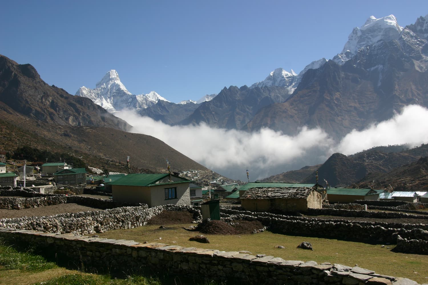 Steinumfriedete Felder und grün gedeckte Häuser von Khunde, in der Ferne die Ama Dablam